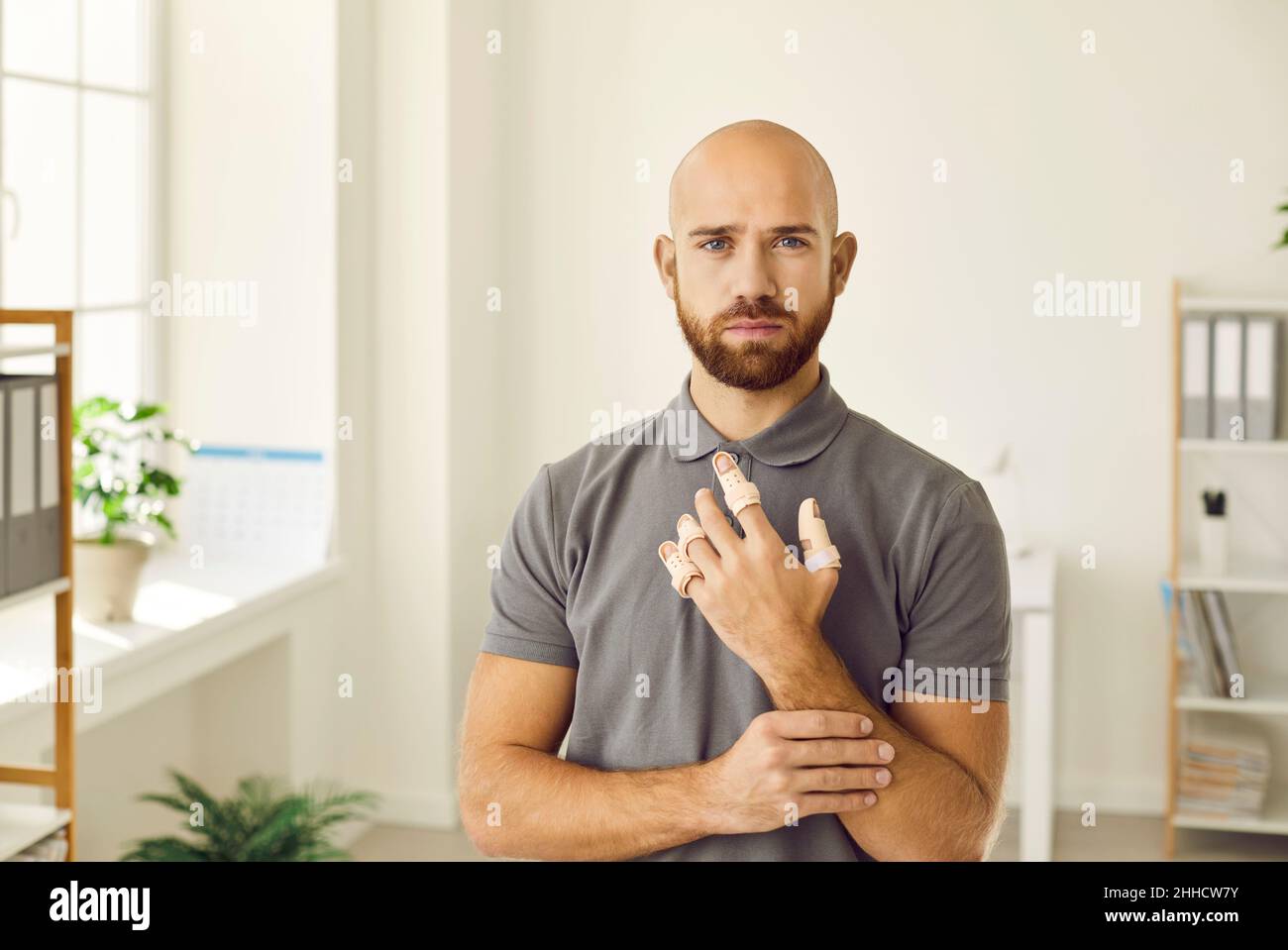 Portrait of sad man who has hurt his fingers and is now wearing adjustable finger splint braces. Stock Photo