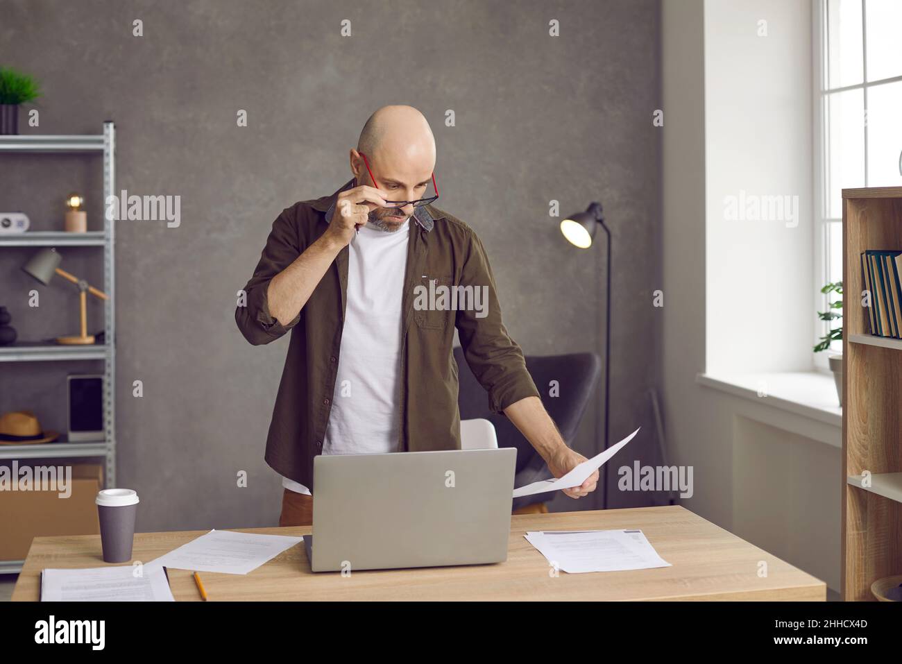 Man looks in surprise through his glasses at bills for payment, bank statement or debt on loan. Stock Photo