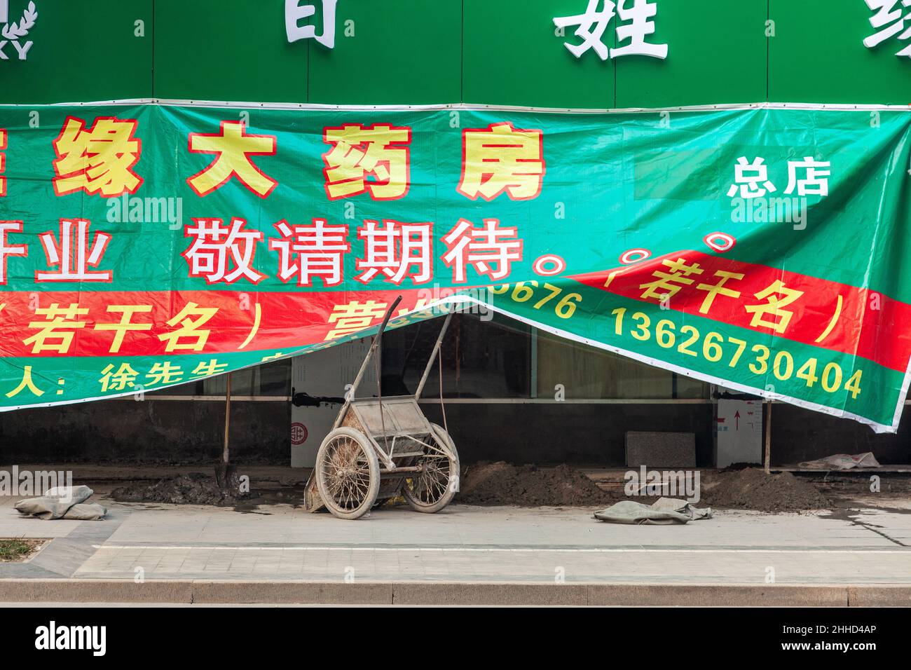 Green and red tarpaulin bearing Chinese characters hiding a worksite, lifted by the arms of a handcart. Jiashan, China Stock Photo