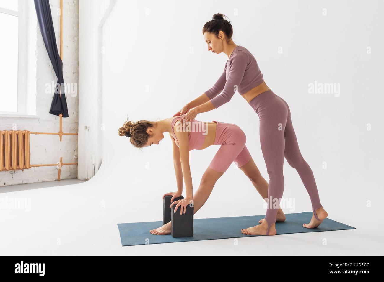 Female trainer helping a student to perform the parshvottanasana exercise correctly, deep stretch pose, personal training in the studio on a white bac Stock Photo