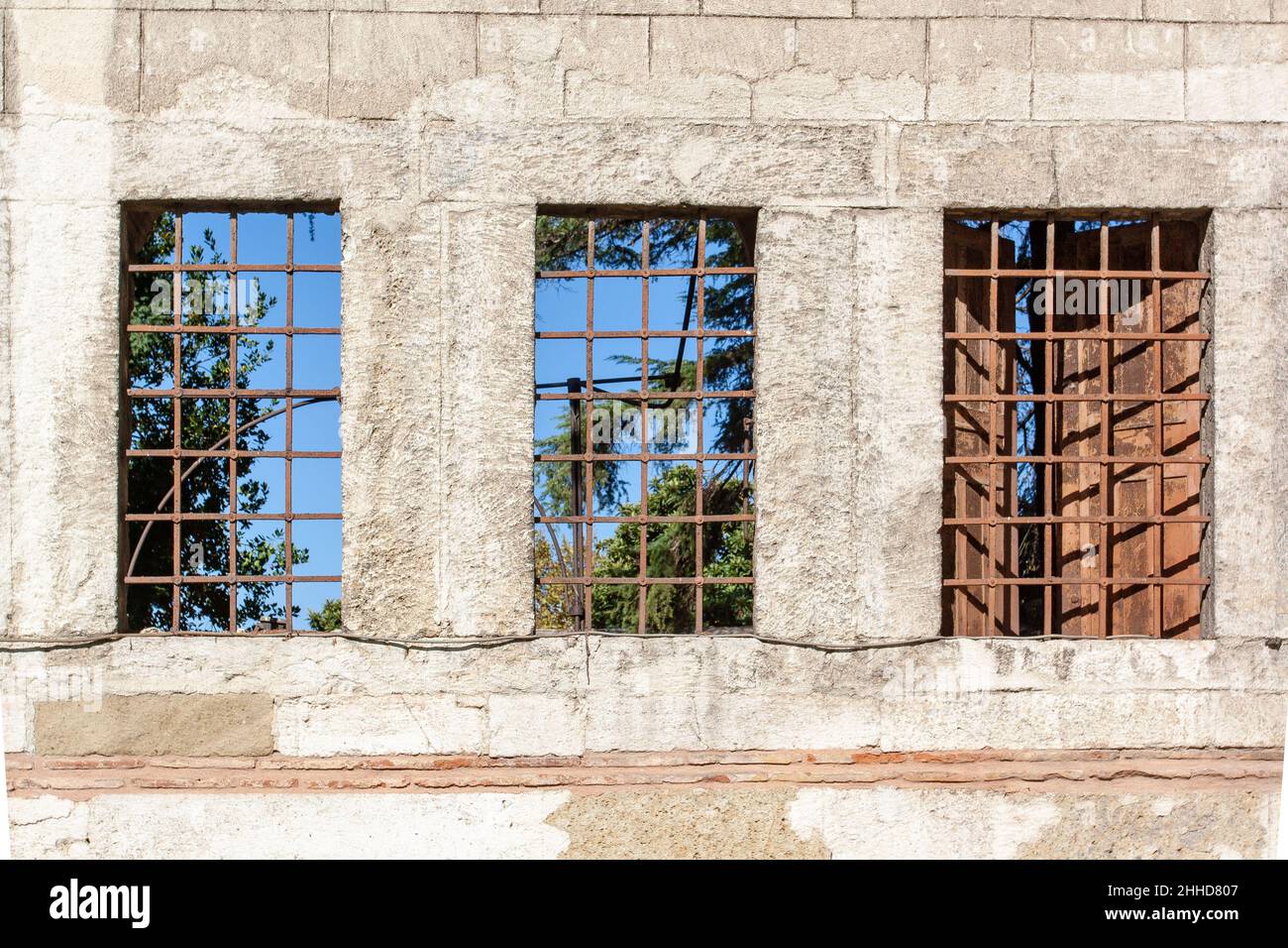 Three windows with bars in block wall. One window has shutters. Stock Photo