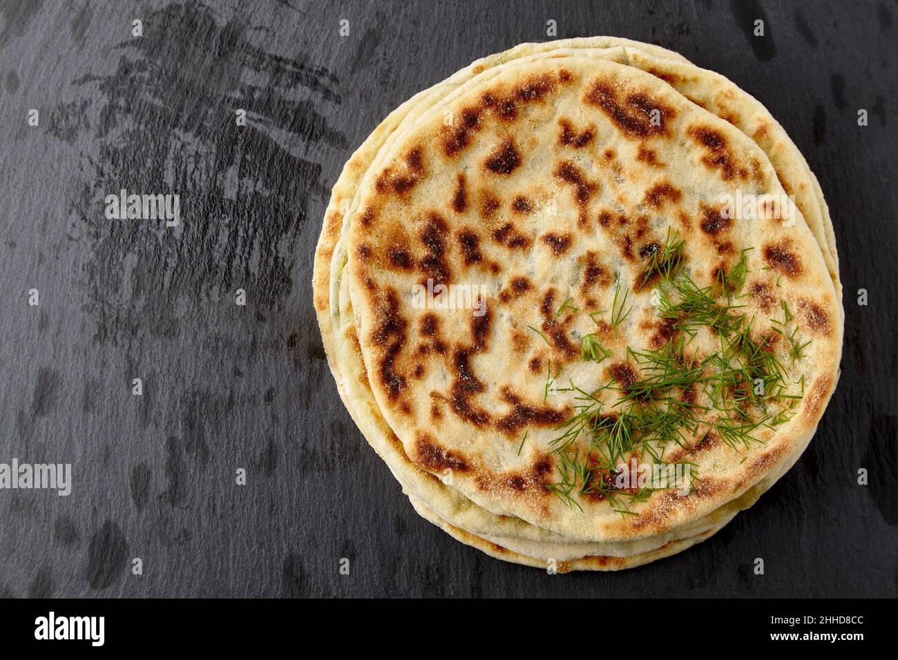 Flatbread with cheese and herbs on a dark stone table Stock Photo