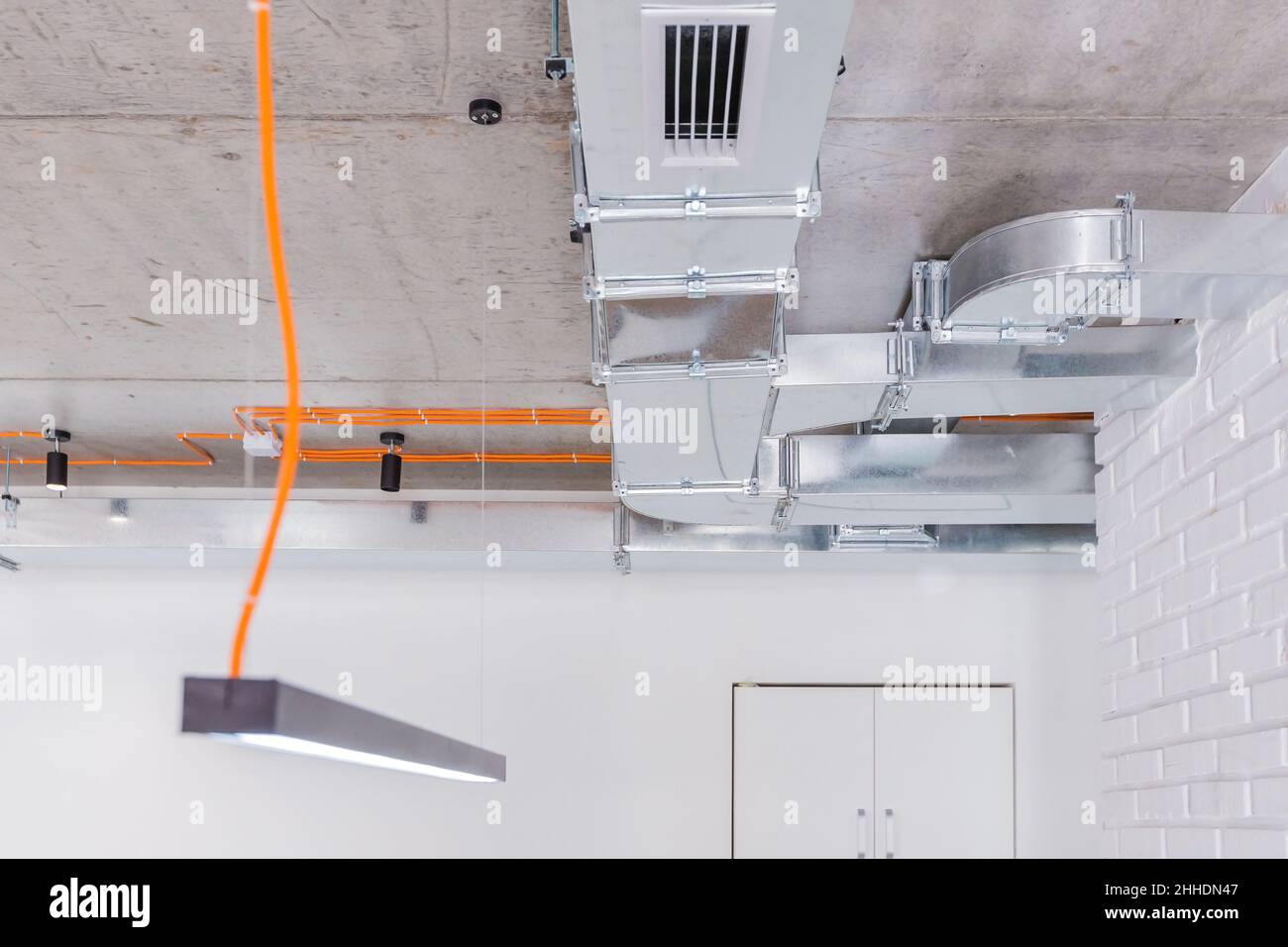 Concrete ceiling with orange electrical wiring and luminaires with ventilation ducts Stock Photo
