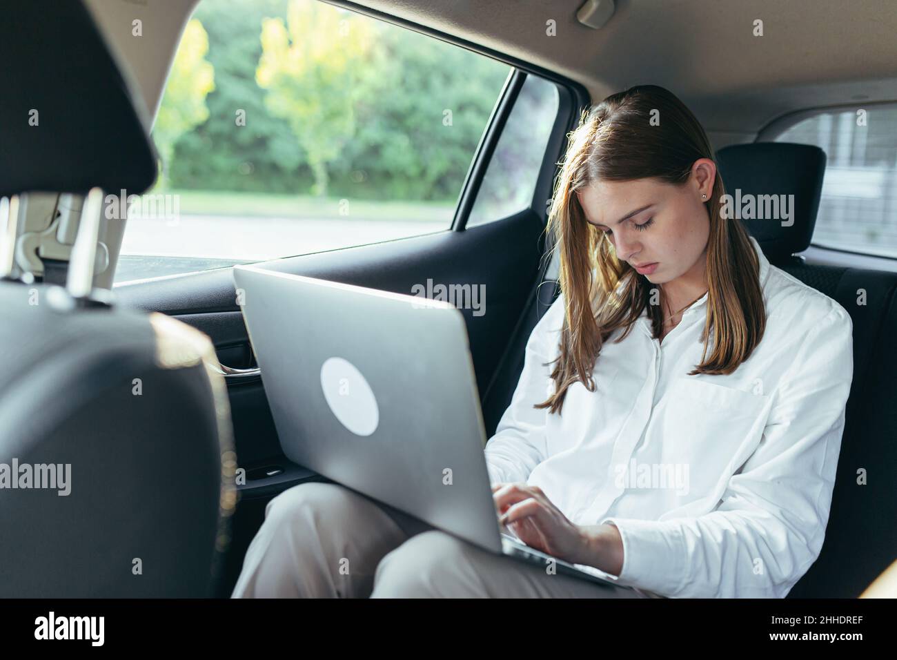 Tired female car passenger holding laptop in hands Stock Photo