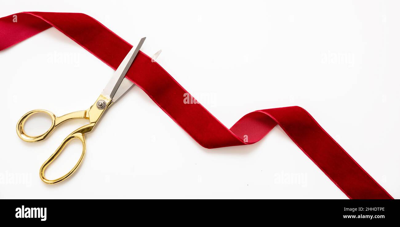 Inaugural invitation, business launch concept, Grand opening, ribbon cut, Gold scissors cutting red velvet ribbon on black background, copy space Stock Photo