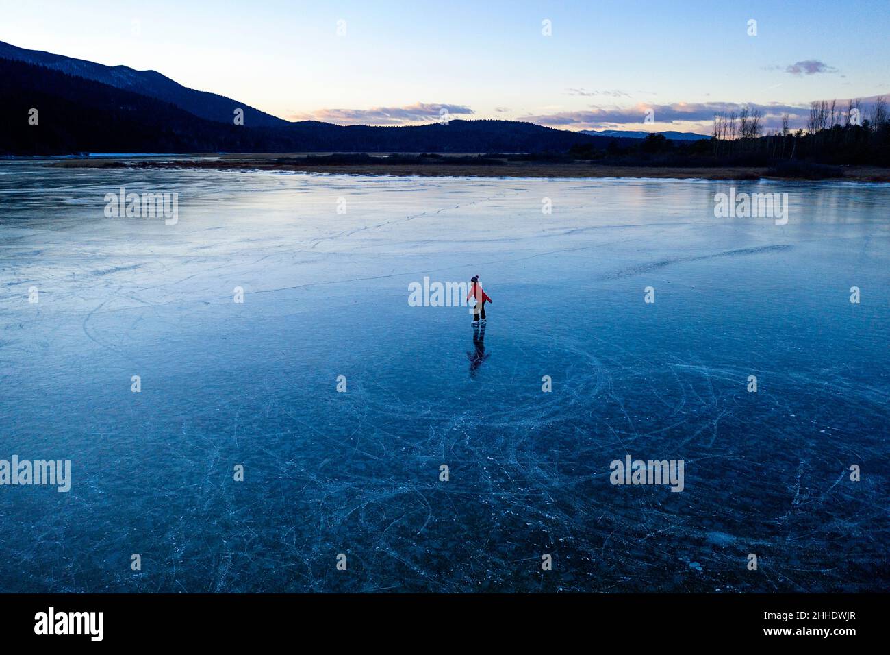 Woman ice skating on frozen intermittent lake Cerknica, Slovenia at sunset Stock Photo