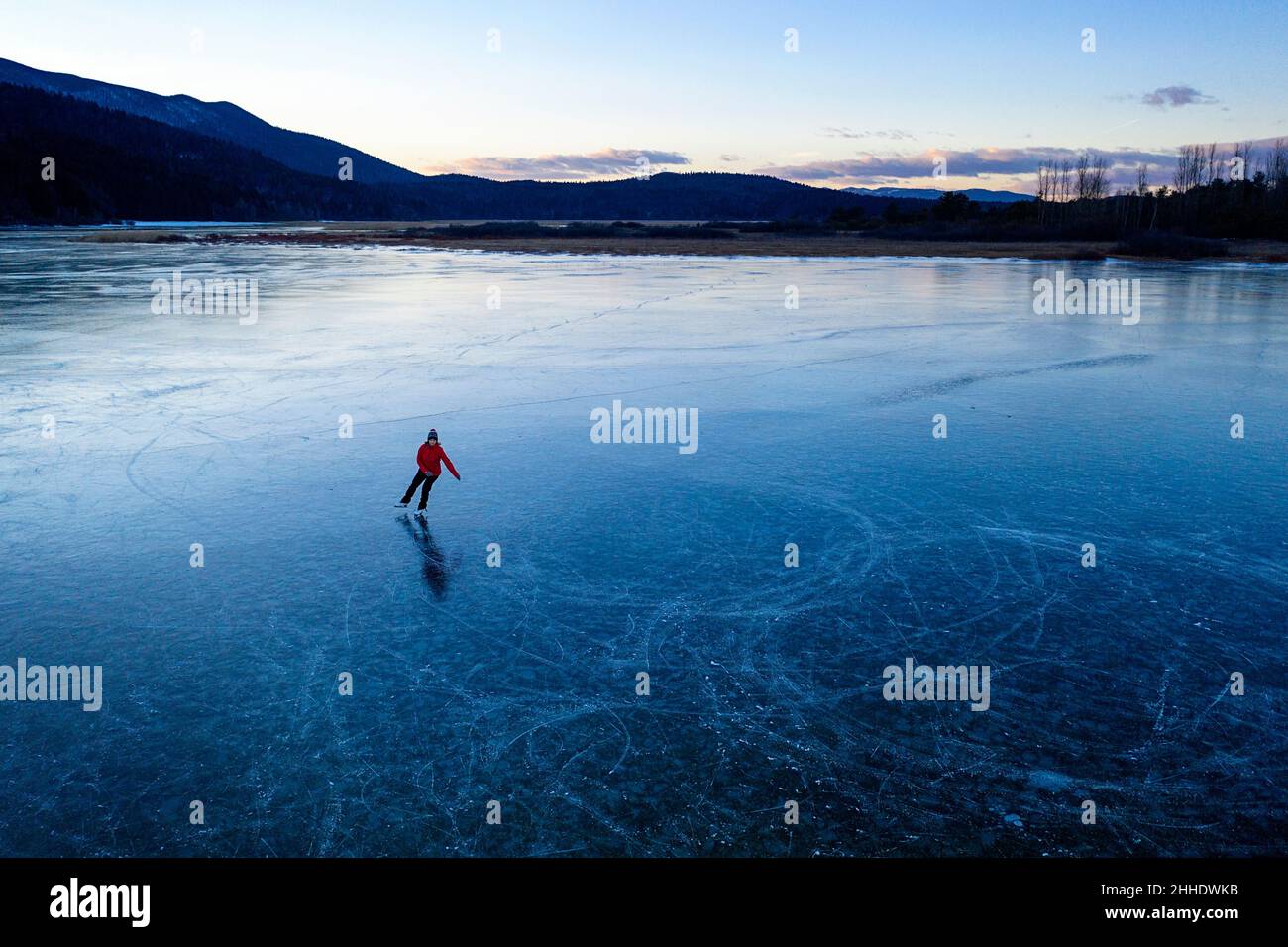 Woman ice skating on frozen intermittent lake Cerknica, Slovenia at sunset Stock Photo