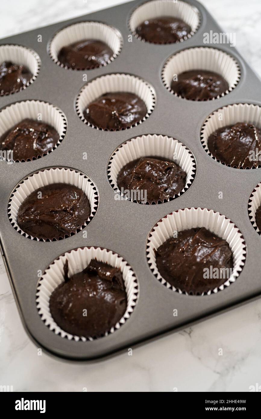 Scooping cake batter with dough scoop into cupcake foil liners to bake