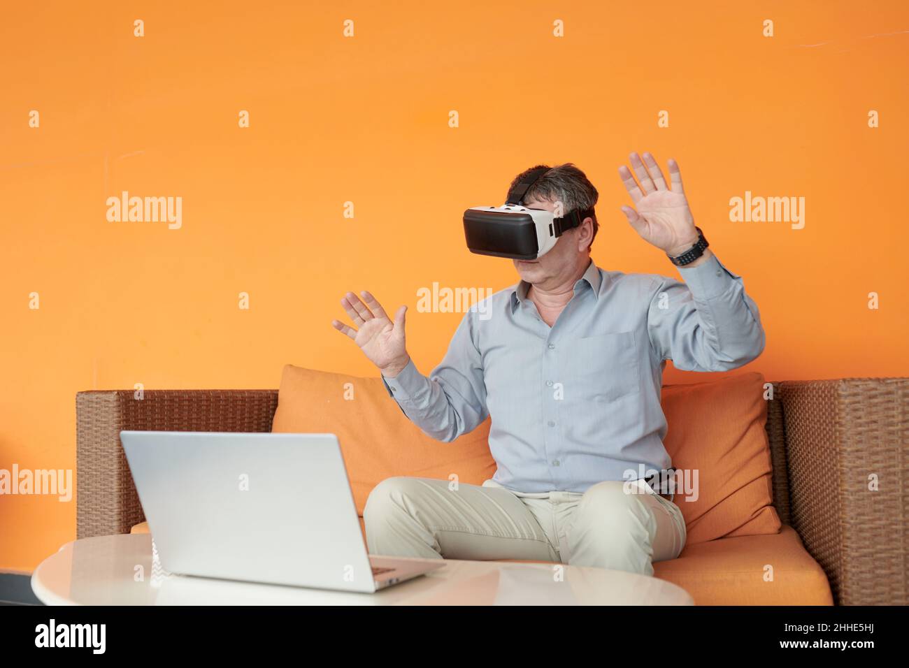 Senior businessman sitting on sofa in virtual reality glasses and testing new application Stock Photo