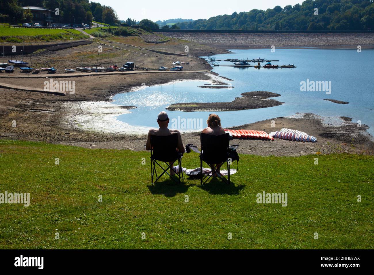 Llandegfedd Reservoir lake low water level 2 people in deckchairs with backs to camera on grass, beached yachts, boats trees summer copy space Stock Photo