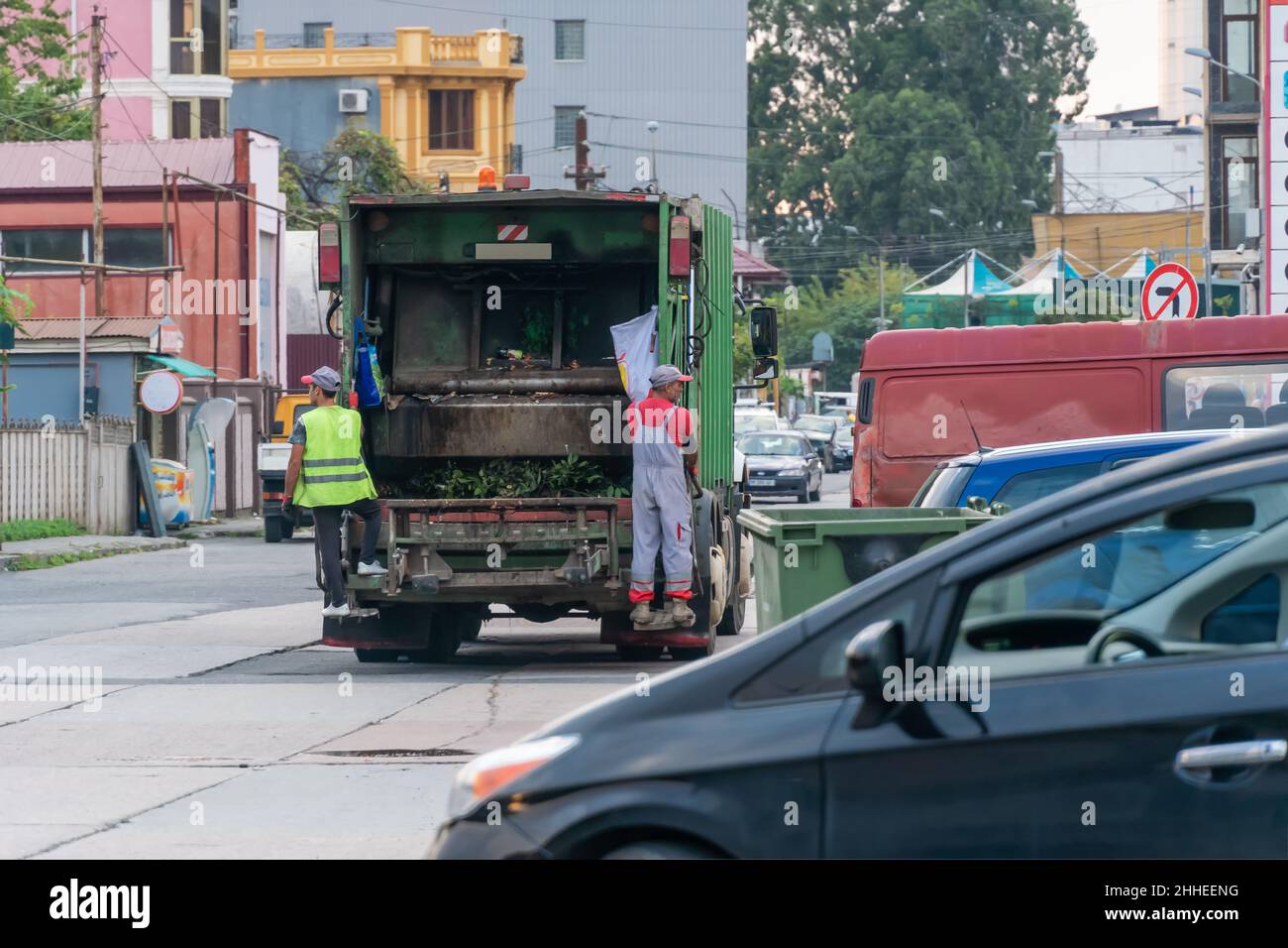 Two garbage men drive a garbage truck and collect garbage from