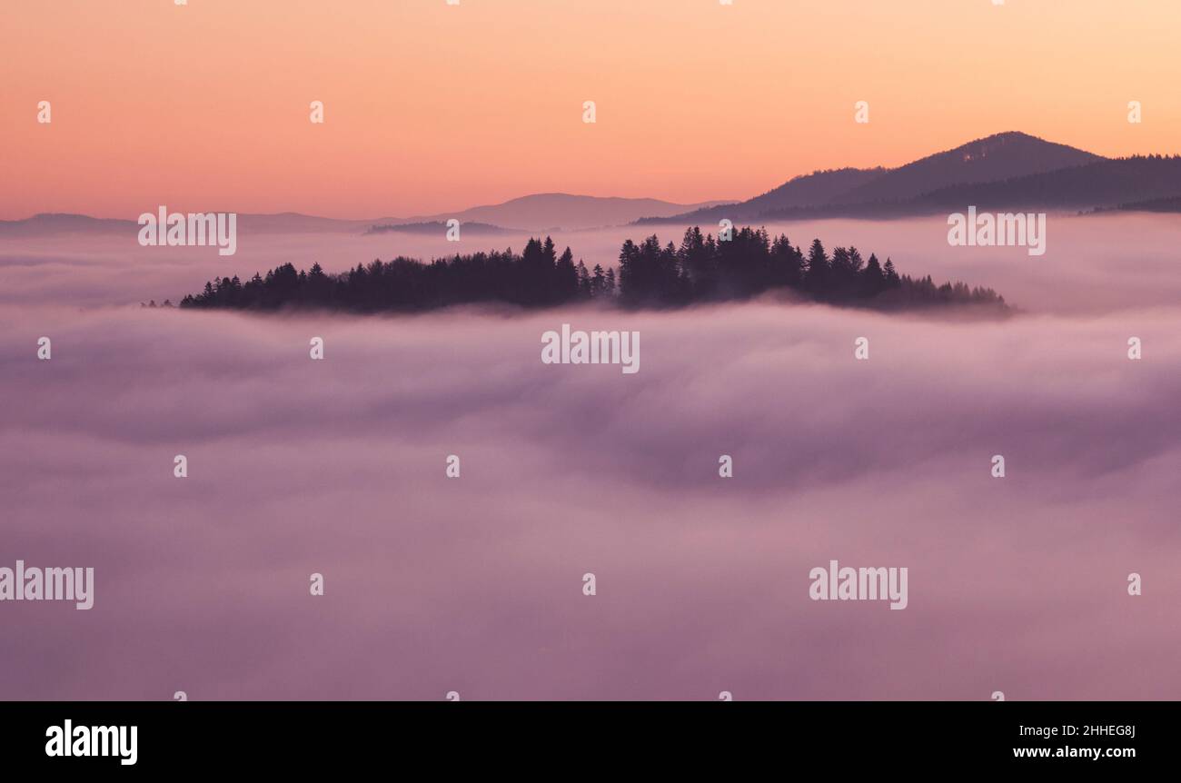 Sunset hidden behind clouds and fog over hills, bright yellow sun on colorful cloudscape, blue violet orange sky. Stock Photo