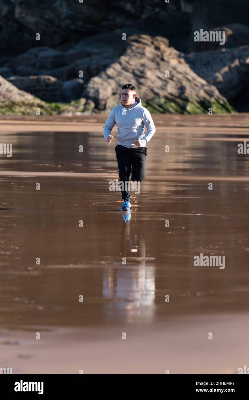 Latin man running at the beach. Goals achievement motivation and loosing weight concept.  Stock Photo