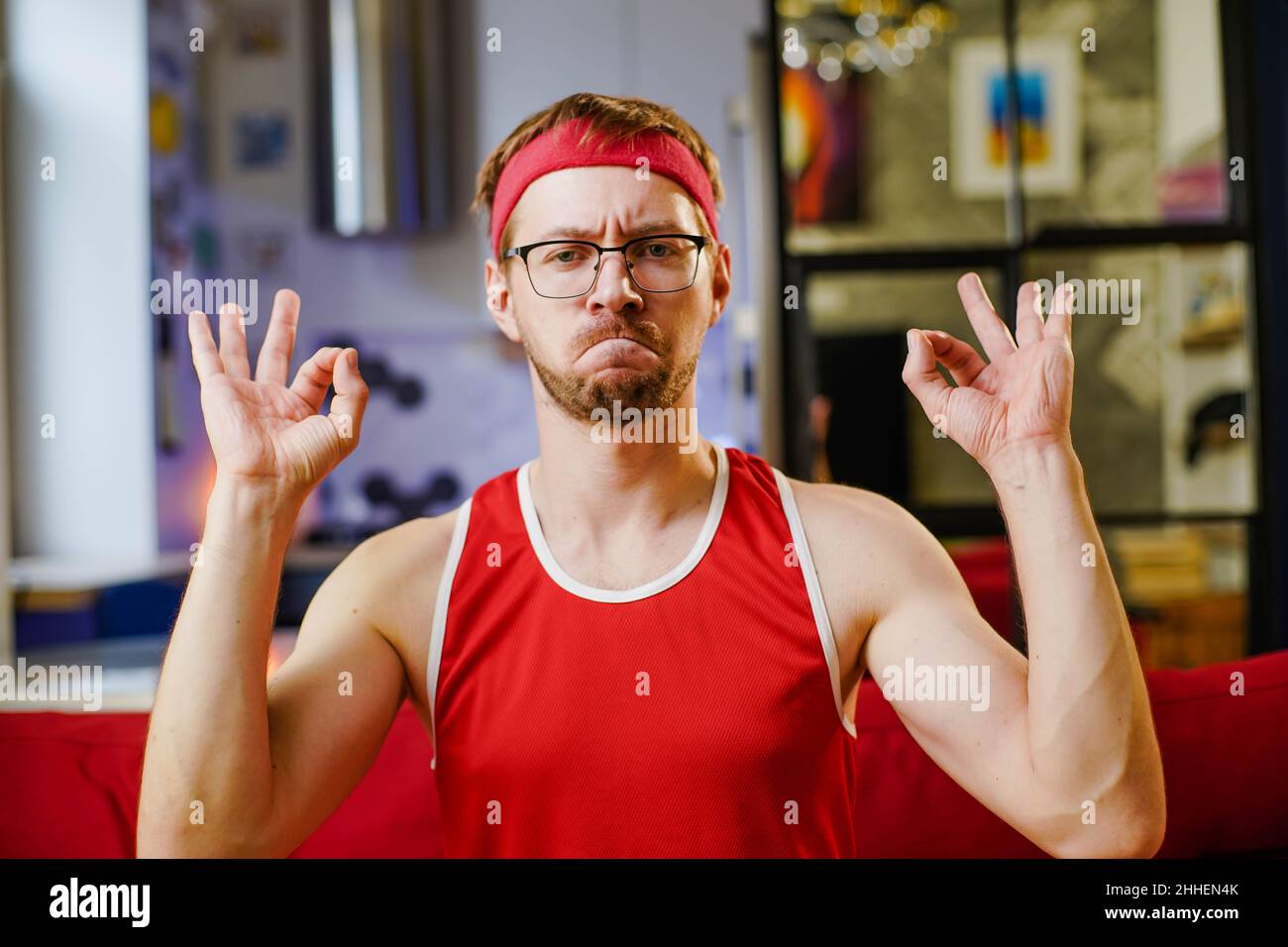 Portrait of funny sportsman in red sportswear making OK sign sitting on  sofa at home Stock Photo - Alamy
