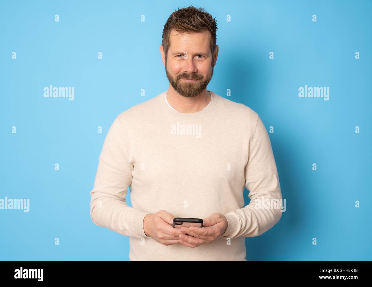 Young bearded man using smartphone standing isolated over blue background. Stock Photo
