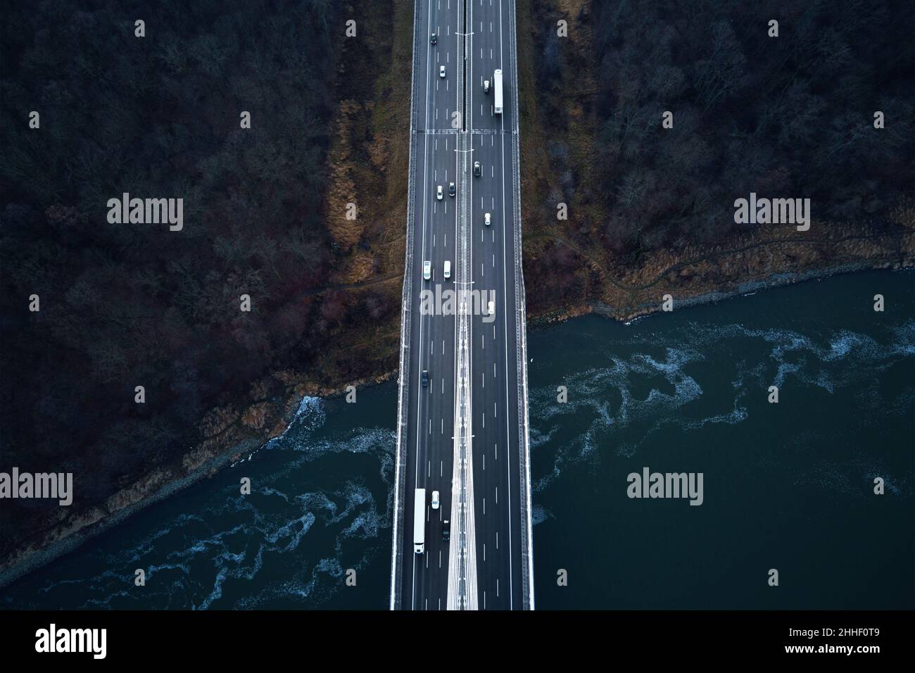 Car traffic moving on highway bridge, aerial view. Countryside road through autumn forest over river. Road trip, delivery and logistic concept Stock Photo