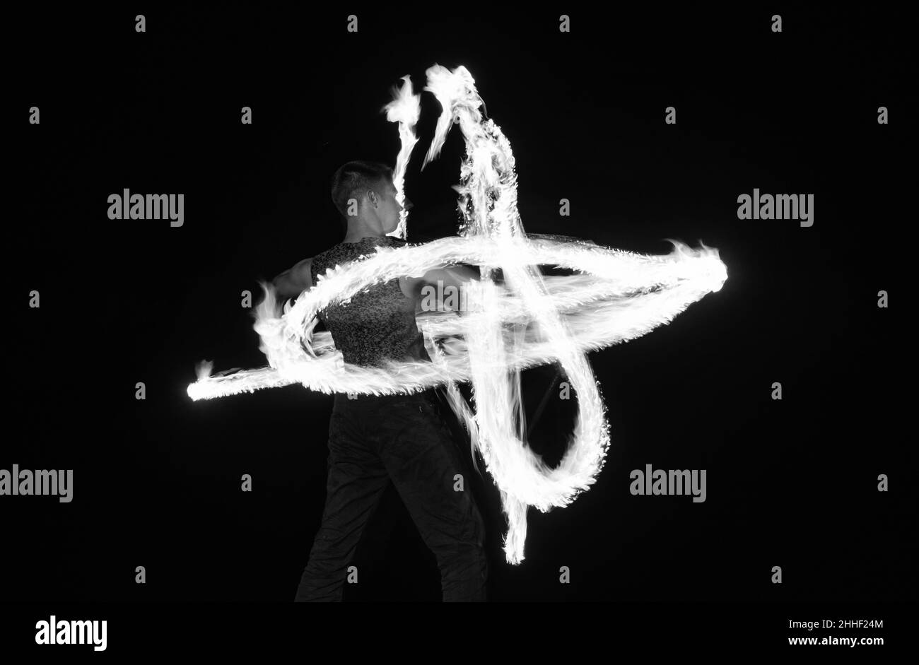 Energetic man performer create sparkling fire patterns twirling burning ...