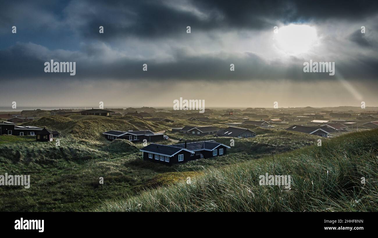 Abendstimmung über einer Ferienhaussiedlung an der dänischen Nordseeküste aus der Vogelperspektive; die Sonne bricht durch eine dunkle Gewitterwolken Stock Photo