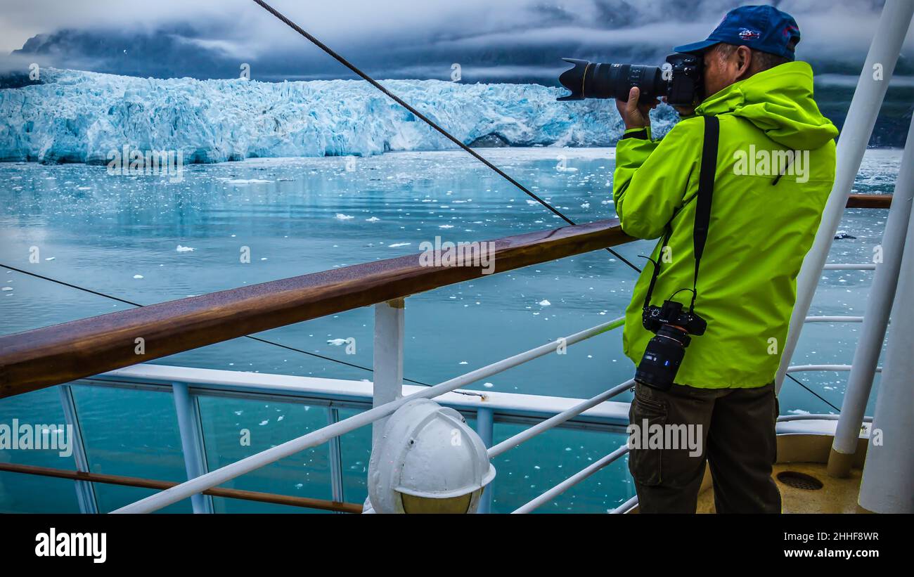 Ein Fotograf in neongelber Windjacke und blauem Cap und zwei Kameras fotografiert an Bord eines Kreuzfahrtschiffs Gletscher in der Glacier Bay Stock Photo