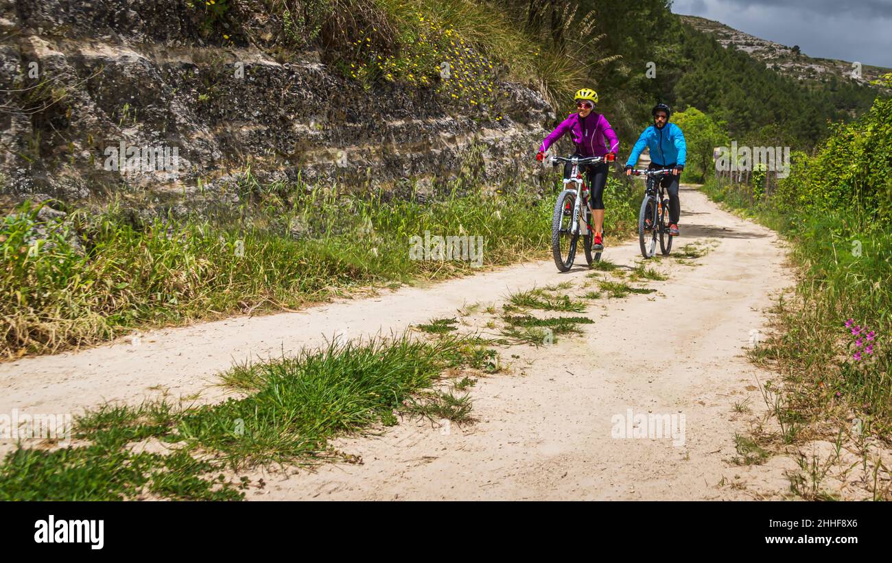 Zwei Biker im Sportdress (pink und hellblau) und Fahrradhelm fahren durch das Val di Noto auf Sizilien Stock Photo