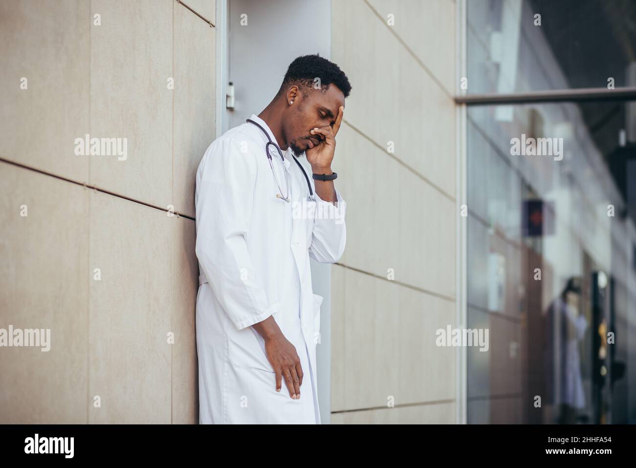 male doctor at the clinic holding his head has health problems and tired after a hard day, depressed did not get the desired result, afro american doc Stock Photo