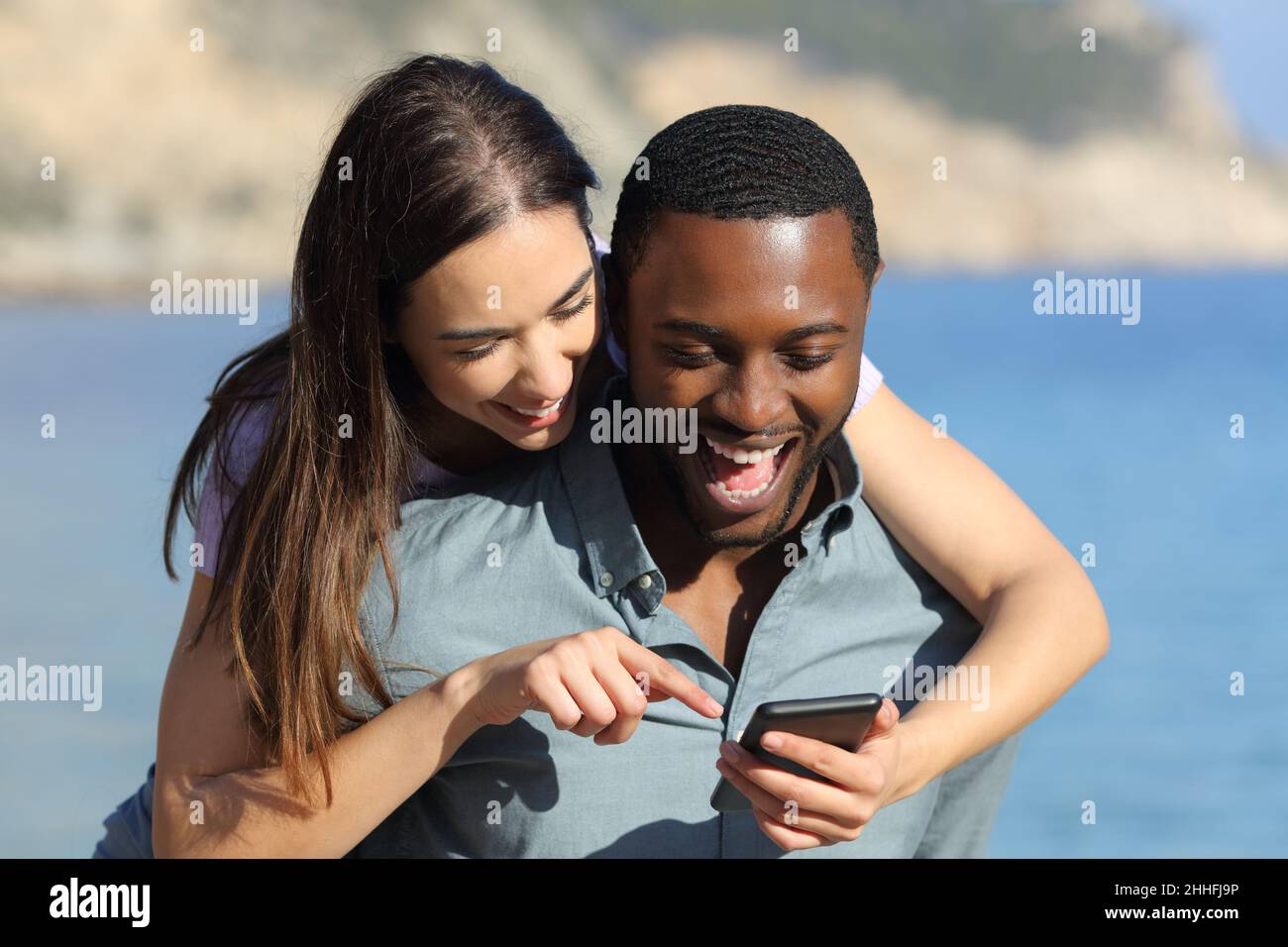 Front View Portrait Of An Interracial Couple Checking Phone Enjoying Together On The Beach On