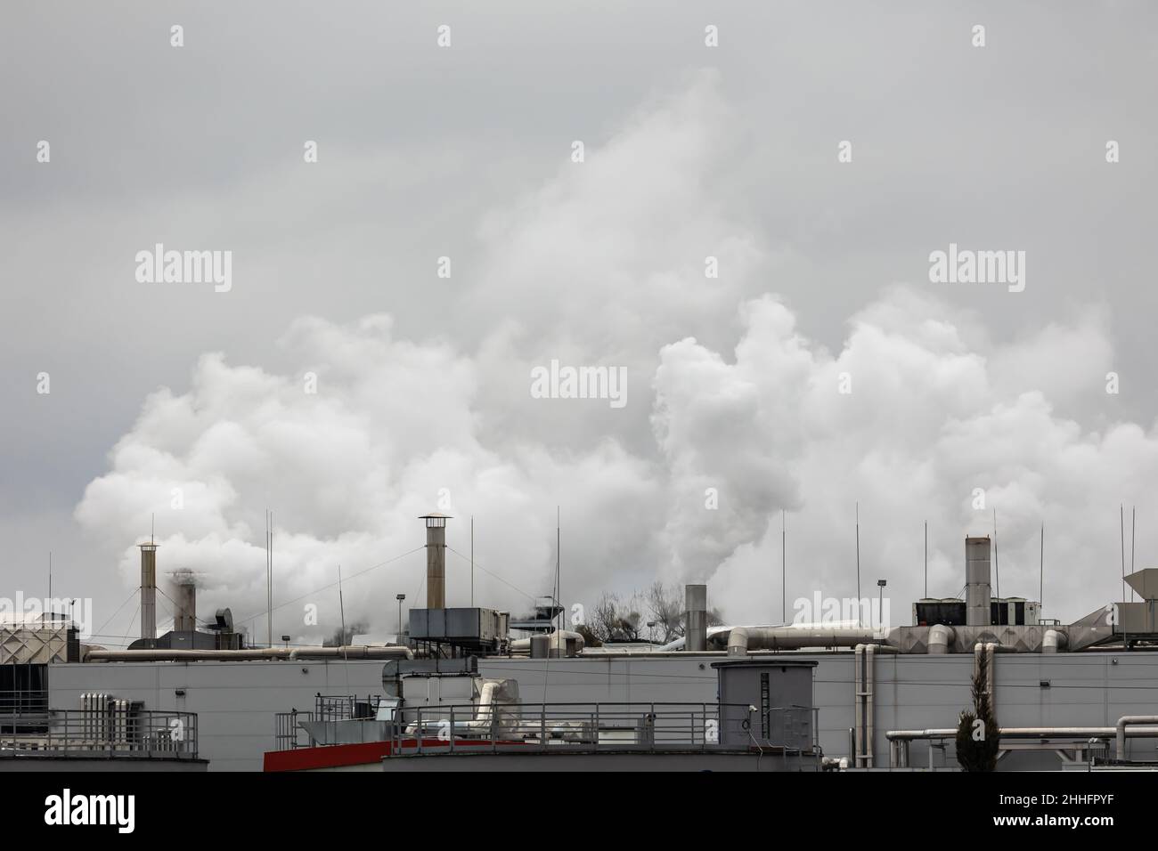 Puffs of steam coming out of chimneys on the roof of an industrial plant. Picture taken on a cloudy day, uniform and soft light. Stock Photo