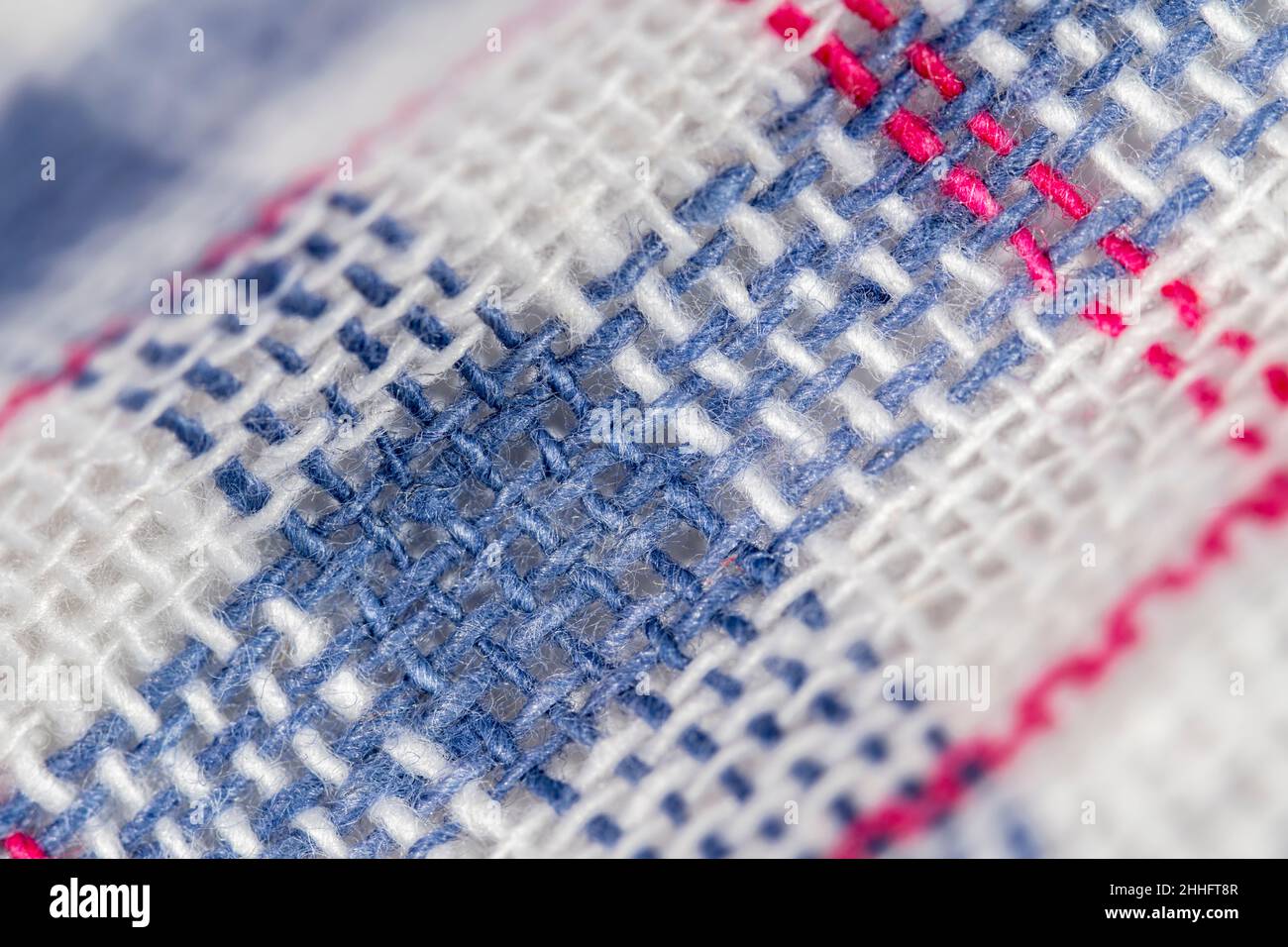 Macro close-up of 100% cotton tea towel fabric, showing cloth warp and weft thread pattern and coloured stitching. Stitched line, rows of stitches. Stock Photo