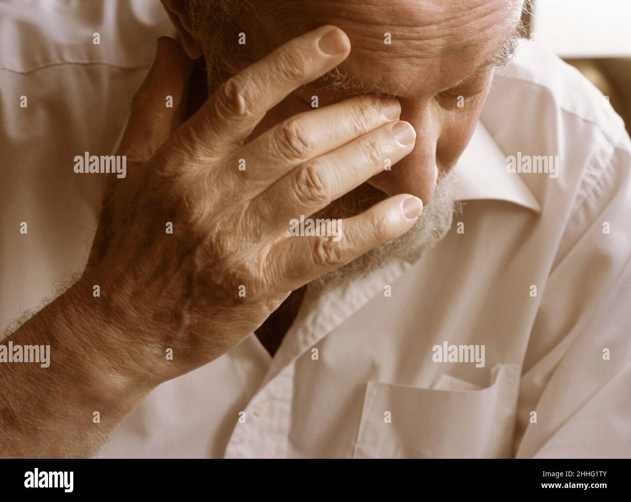 Aging, anxiety and emotion. Elderly man with his hand to his face. Portrait of a mature tired and serious male deep in thought. Stock Photo