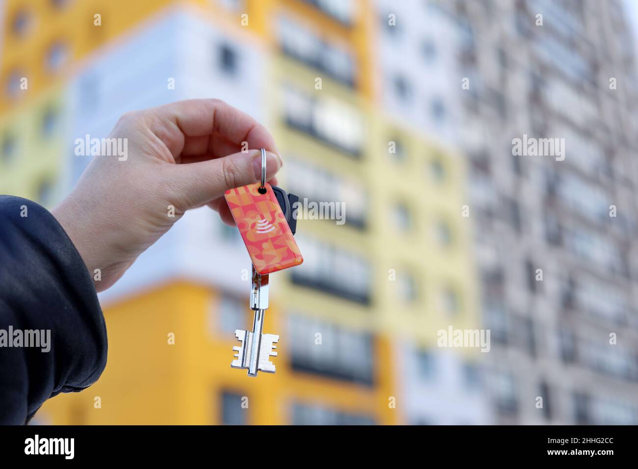 House purchase in winter, woman holding house keys on background of new apartment building. Real estate agent, moving home or renting property Stock Photo