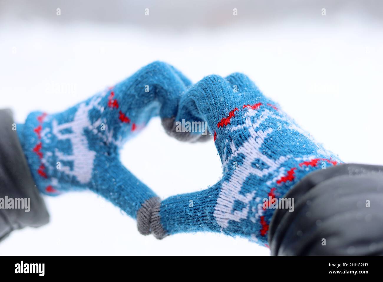 Hands in knitted gloves folded in the shape of a heart on snow background. Declaration of love, concept of Valentine's day, winter weather Stock Photo