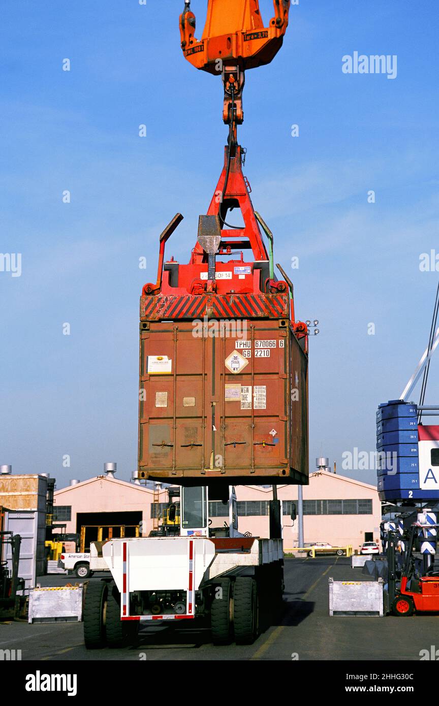 Shipping container suspended over trucking vehicle in port. Crane moving a cargo container. Commercial dock loading area. Infrastructure USA Stock Photo