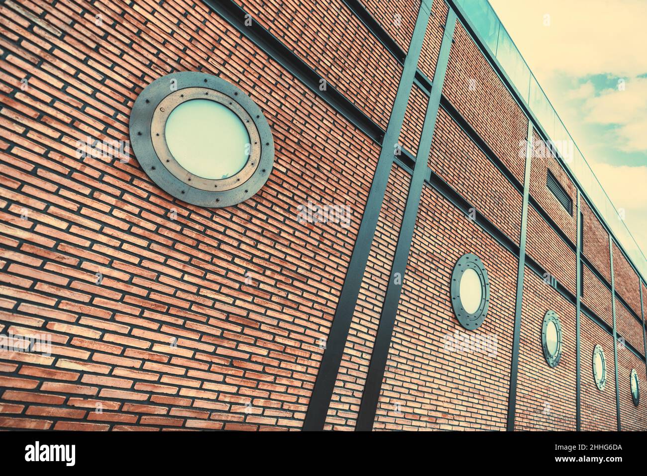 A perspective view of a modern brick wall of a contemporary building with steel beams and futuristic portholes or illuminator windows in a steampunk s Stock Photo