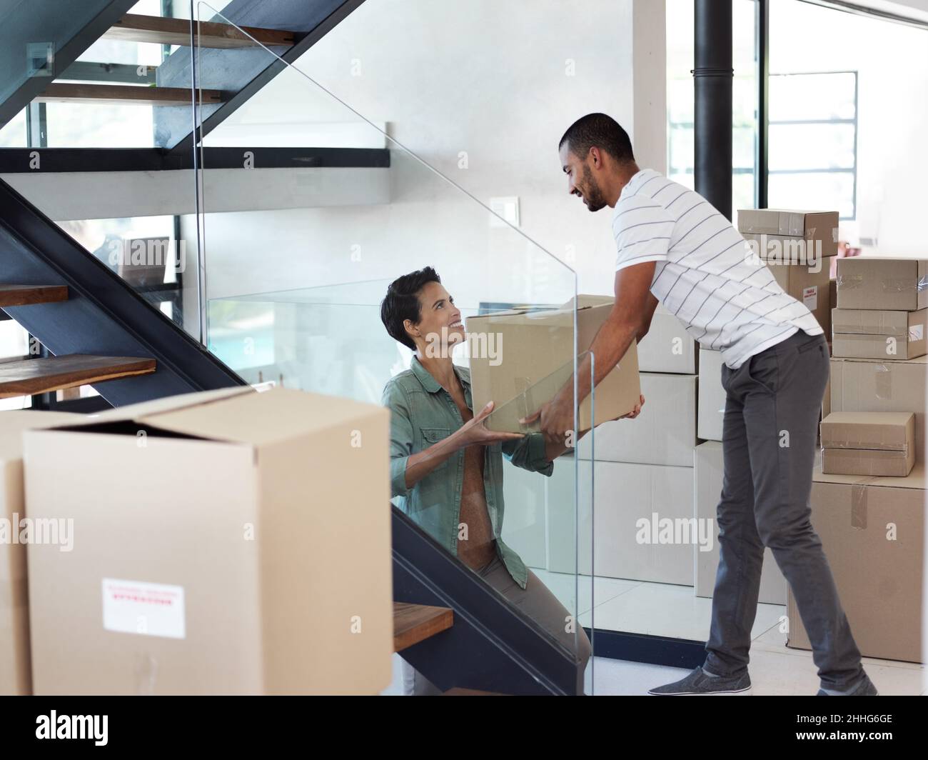 They make moving house look easy. Shot of a happy young couple passing boxes to each other while moving into their new home. Stock Photo