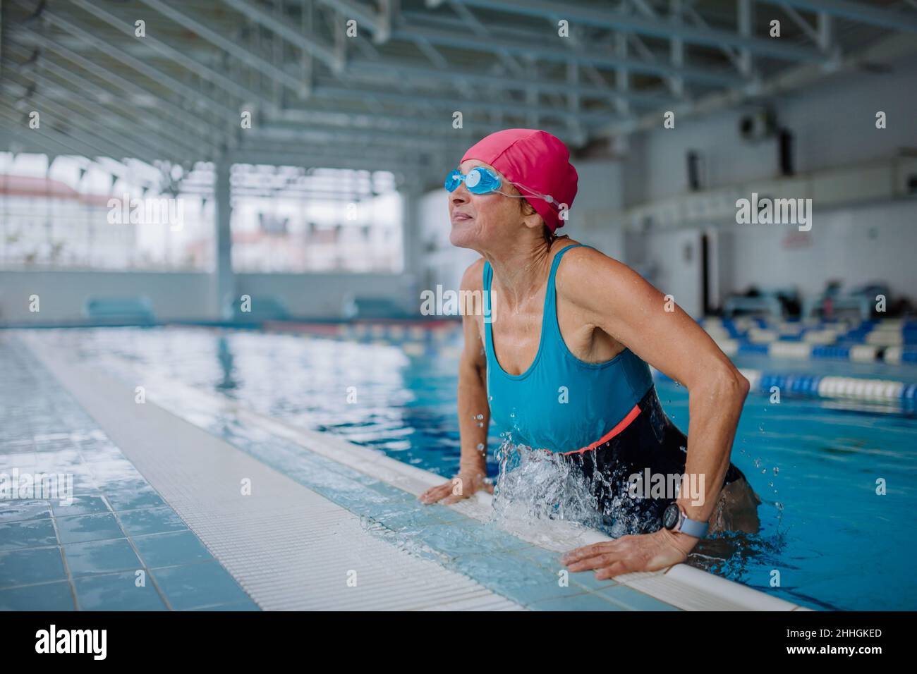 Happy senior woman getting out of the swimming pool indoors. Stock Photo