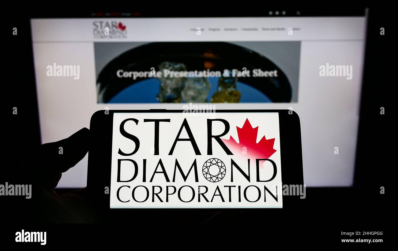Person holding cellphone with logo of Canadian mining company Star Diamond Corporation on screen in front of webpage. Focus on phone display. Stock Photo