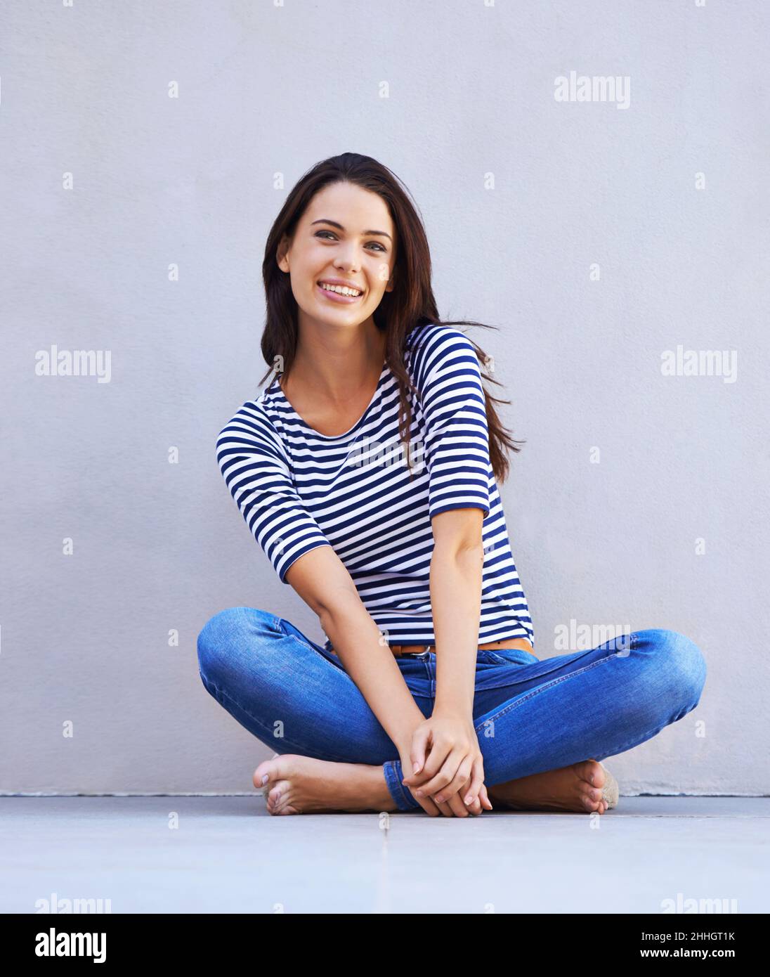Happy being me. Full-length shot of a beautiful young woman sitting cross-legged on the floor. Stock Photo