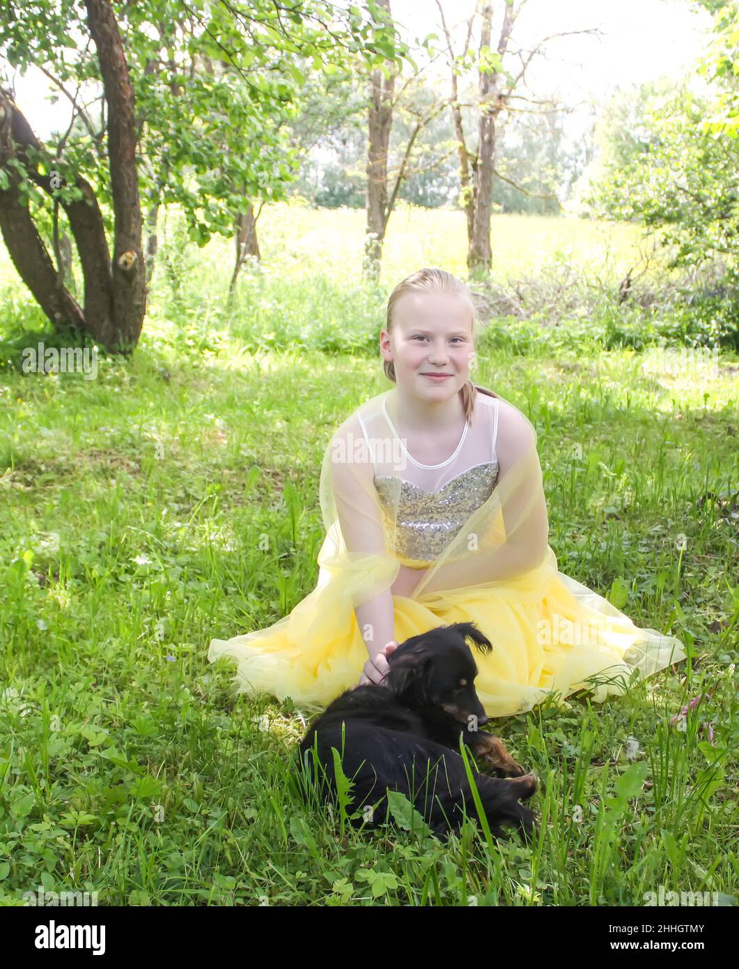 Adorable blonde girl in a yellow dress playing with her dog in a summer ...
