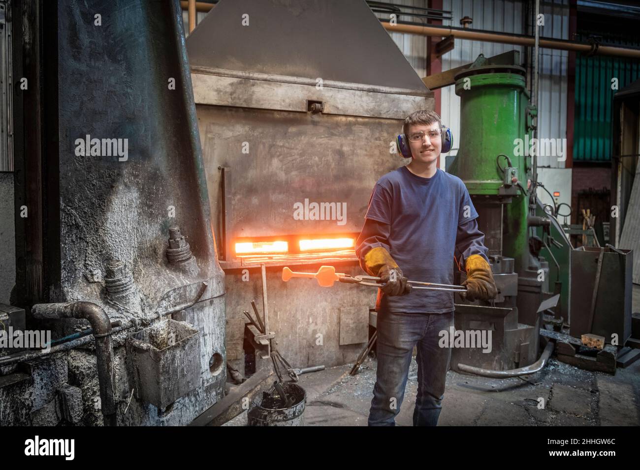Portrait of apprentice engineer with hot titanium part in industrial forge Stock Photo
