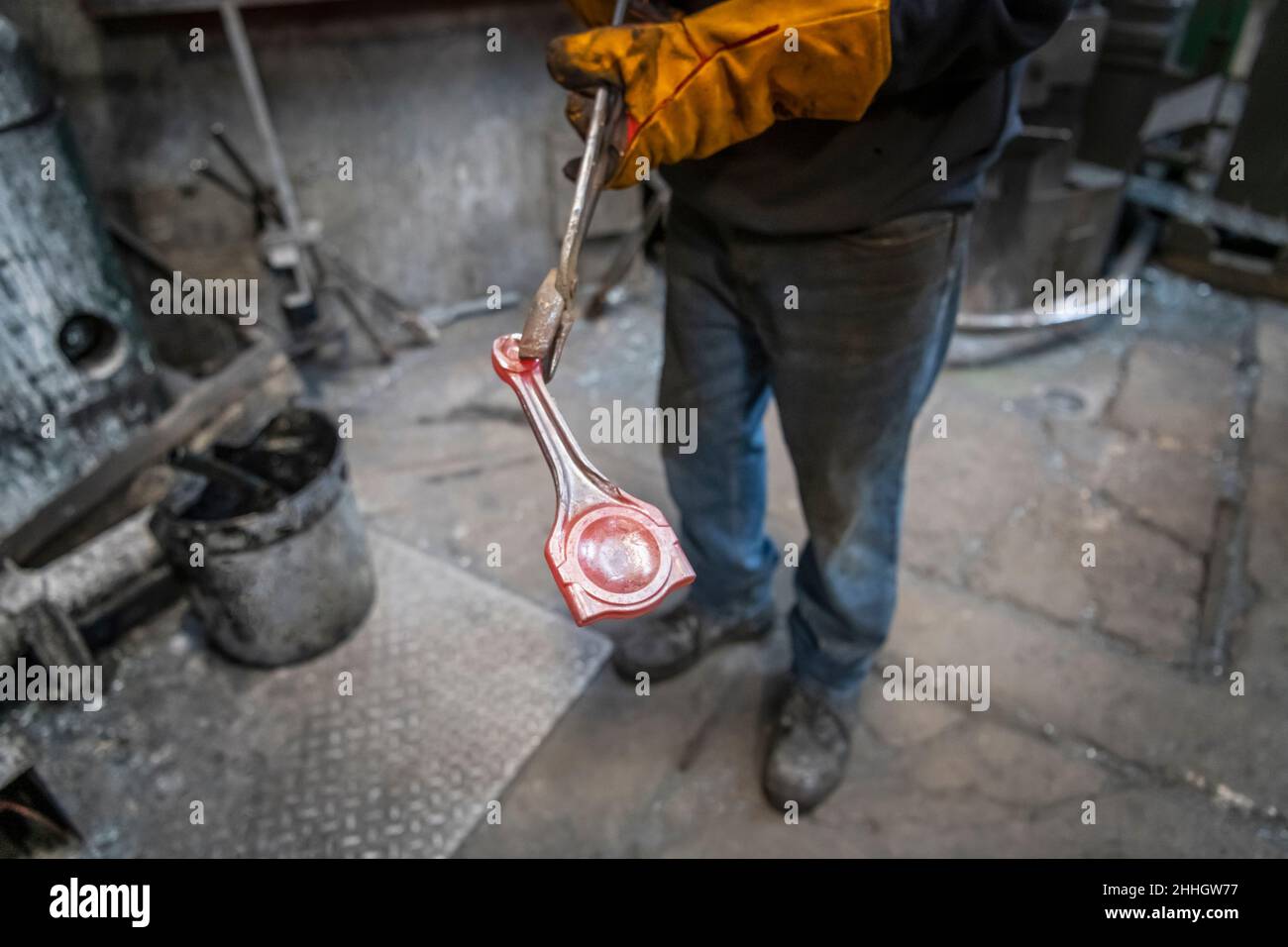 Worker holding hot titanium forged part in industrial forge Stock Photo