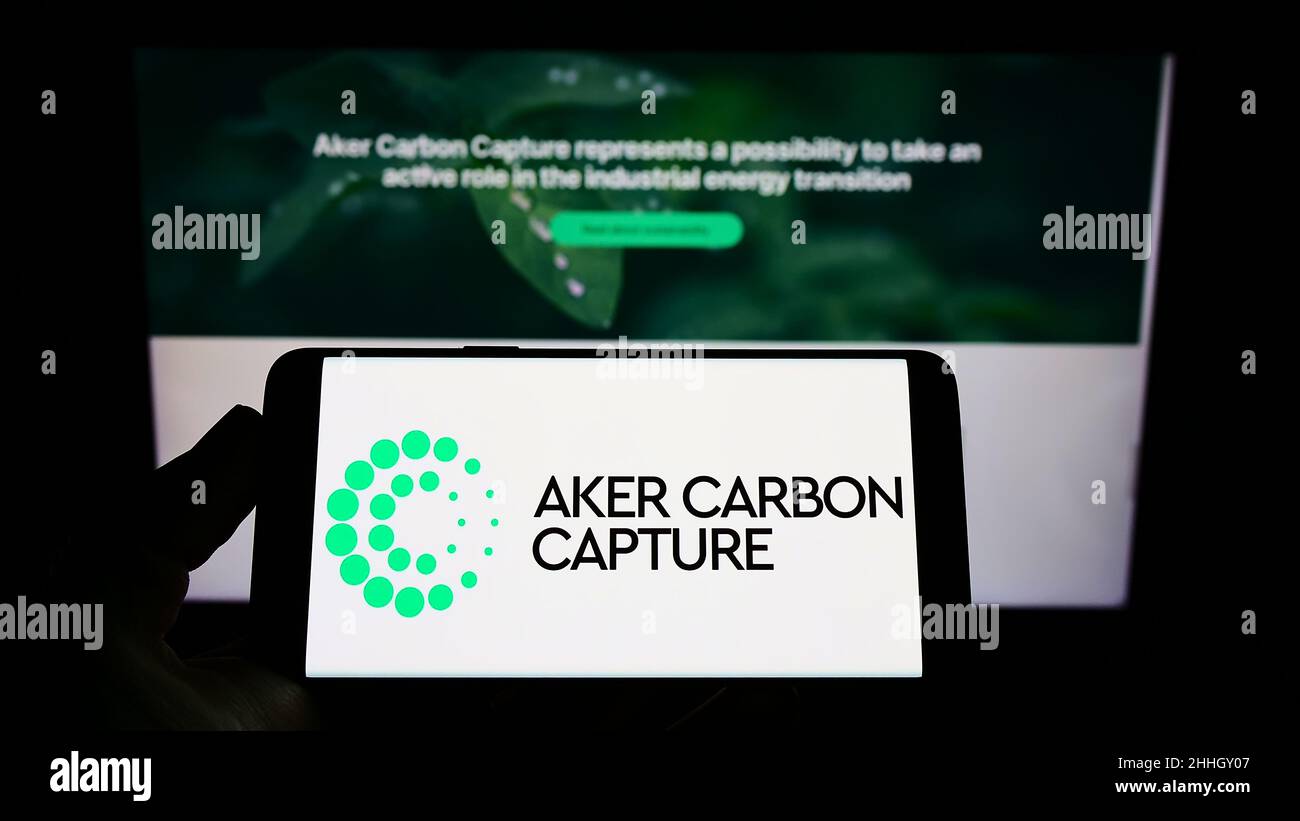 Person holding mobile phone with logo of Norwegian company Aker Carbon Capture ASA on screen in front of web page. Focus on phone display. Stock Photo