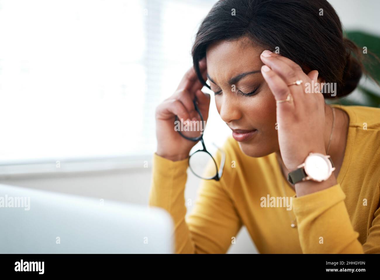 Have I overdone it. Cropped shot of an attractive young woman sitting in her home and suffering from a headache while using her laptop. Stock Photo