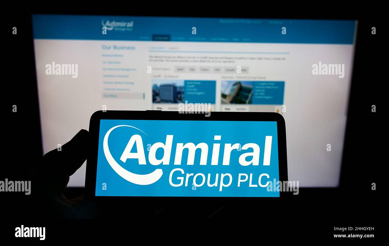 Person holding mobile phone with logo of British insurance company Admiral Group plc on screen in front of web page. Focus on phone display. Stock Photo