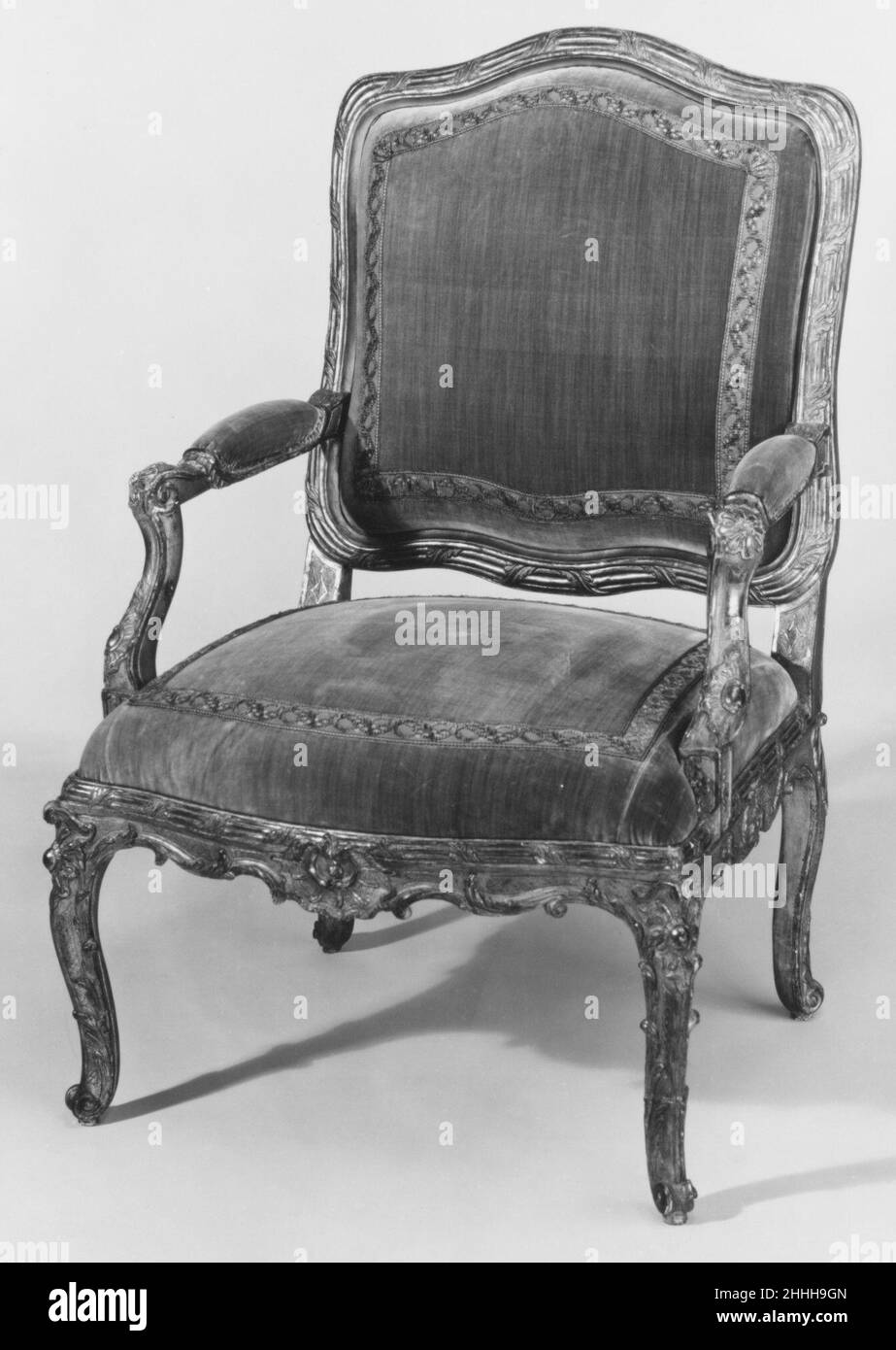 Armchair (one of a pair) ca. 1730 French Carved and gilded frame; flat square back with serpentine sides and slightly arched serpentine top and lower rail, all carved with reeded molding clasped by acanthus leaves; supported above seat rail on short, straight struts pounced with diamond shape; padded arms on serpentine supports set back from fore legs and carved at the top with a floral rosette and at the lower end with a rococo shellwork cartouche; serpentine seat rail carved on upper border with reeded molding clasped by acanthus leaves; shell cartouches carved at center of front and side ra Stock Photo