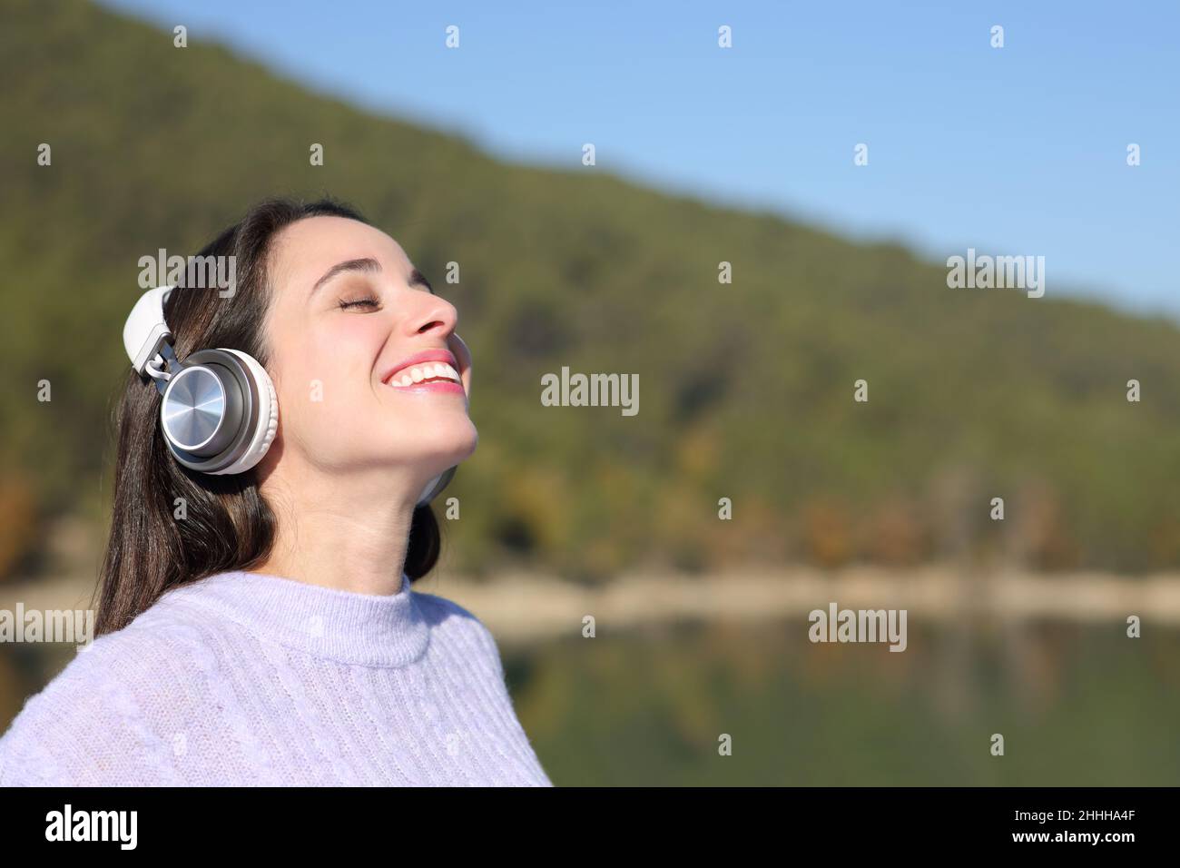 Happy woman meditating with wireless headphones in a beautiful lake Stock Photo