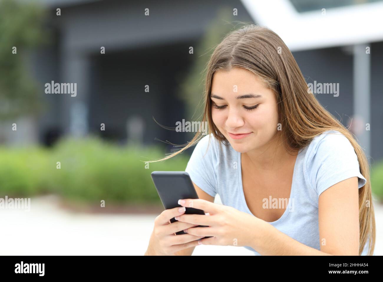 Teenage female checking smart phone sitting alone in the street Stock Photo