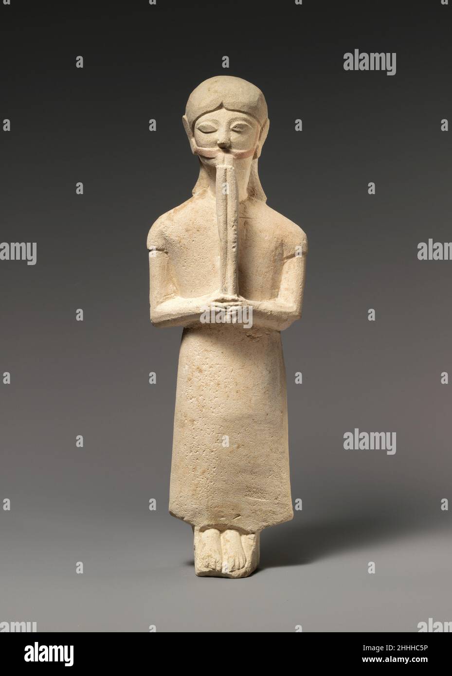 Limestone flute-player 1st half of the 6th century B.C. Cypriot The asymmetrical body of the figure stands on a slanting plinth, barefoot. The arms are long and thin. The figure wears a long, pleatless tunic and holds in each hand a reed of his very long aulos.. Limestone flute-player. Cypriot. 1st half of the 6th century B.C.. Limestone. Archaic. Stone Sculpture Stock Photo