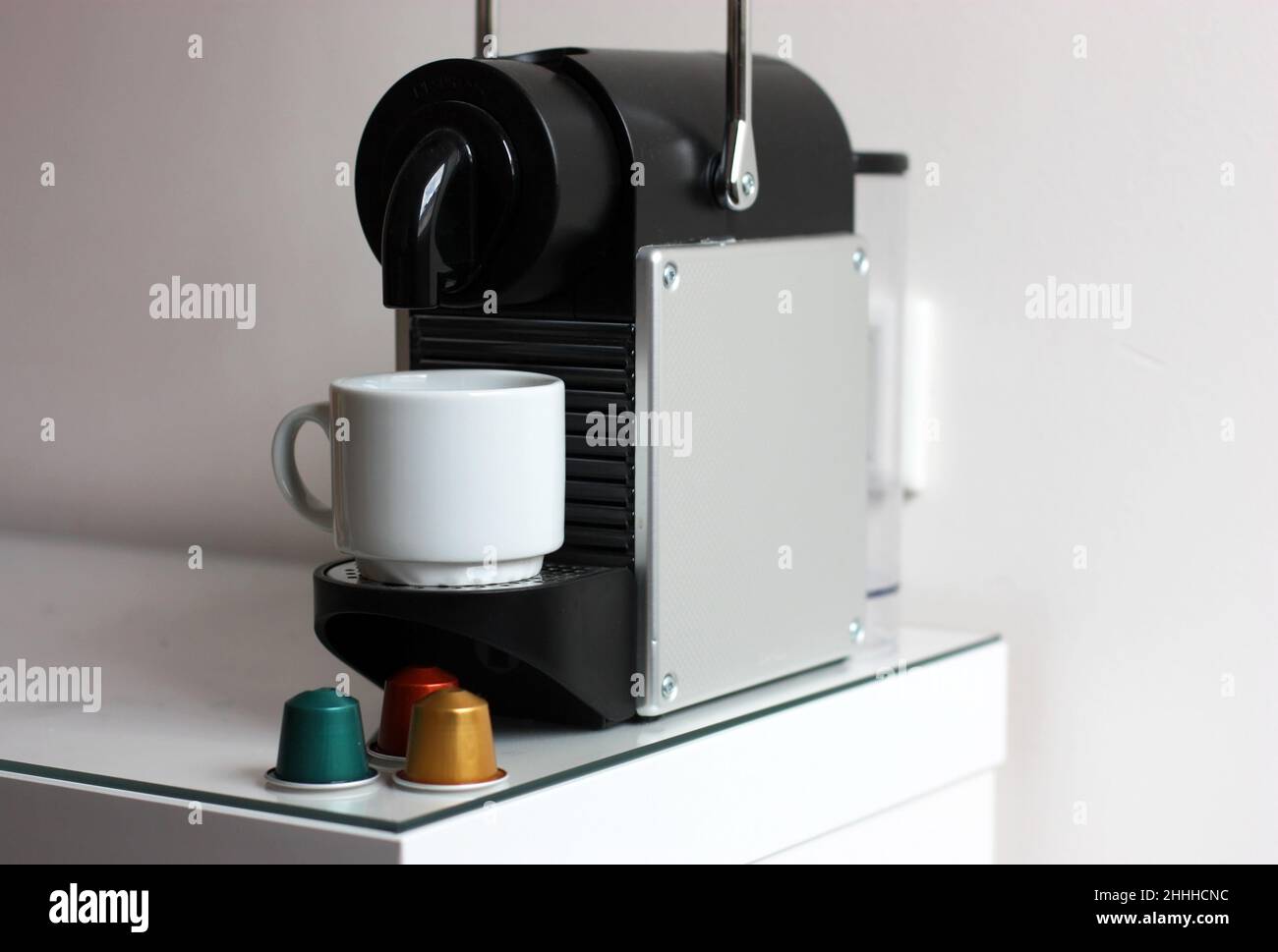 Coffee machine with white cup and coffee capsules against the background of a white wall horizontally. Stock Photo
