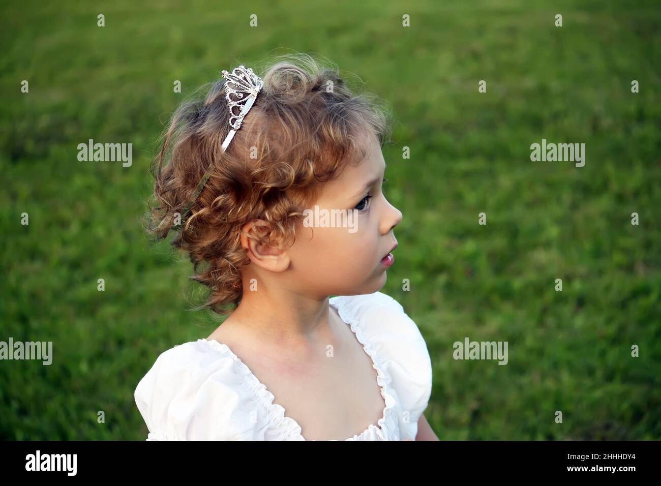 Little girl in white dress with a crown on her head walking outdoors on ...