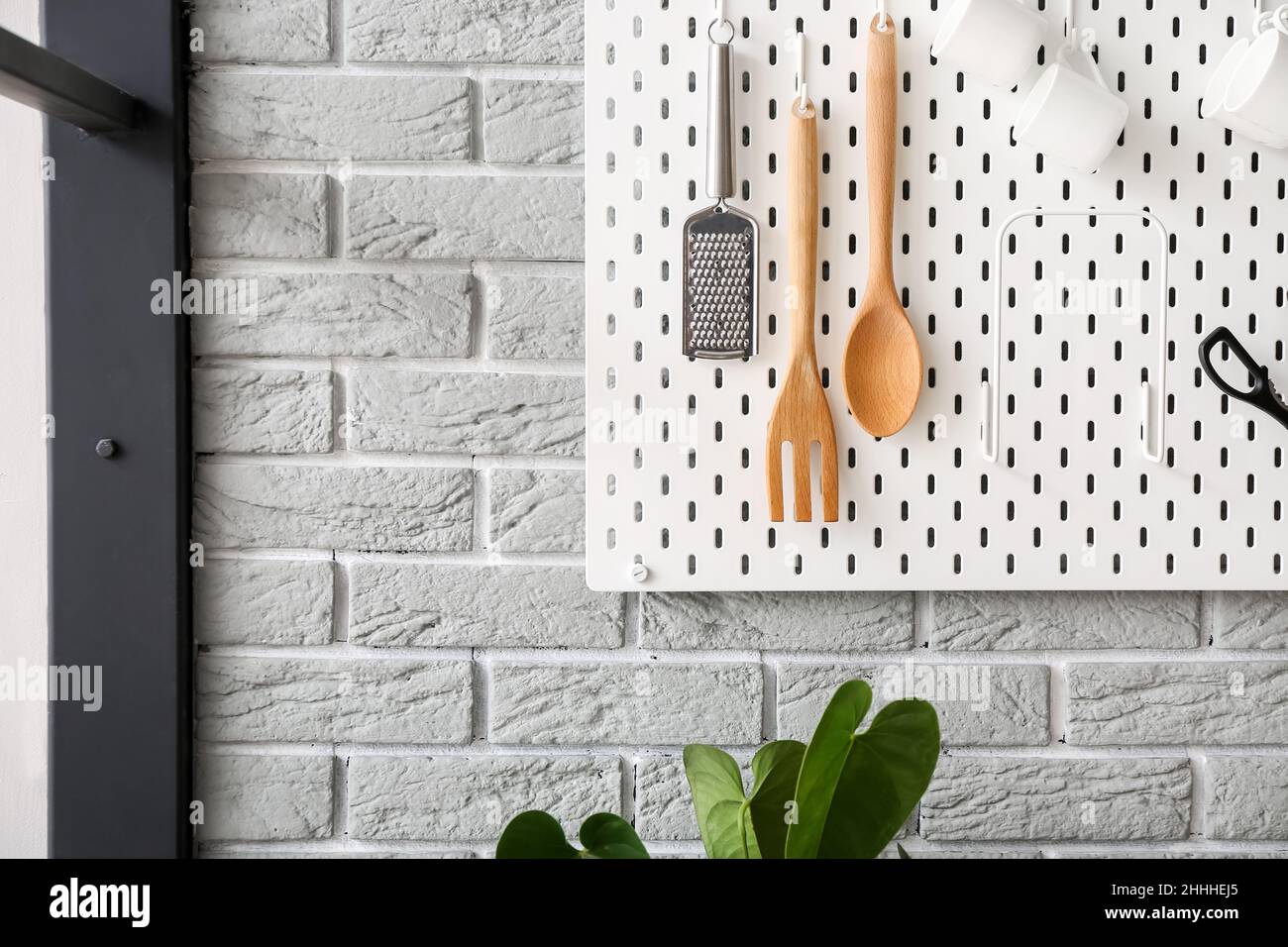 Pegboard with kitchen utensils and cups on grey brick wall Stock Photo